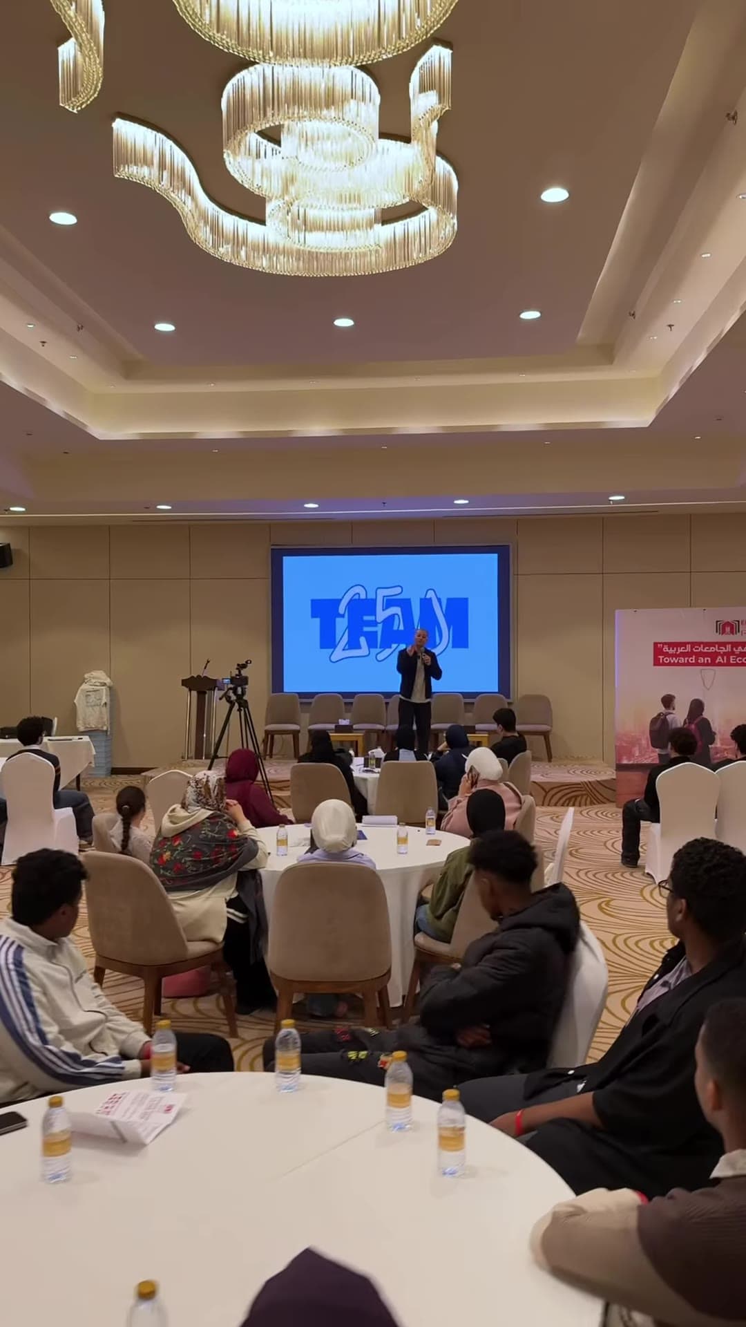 Wide view of the event hall with students at round tables