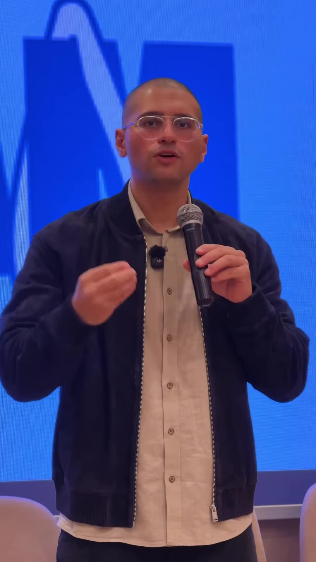 The educator speaking on stage in front of the event screen